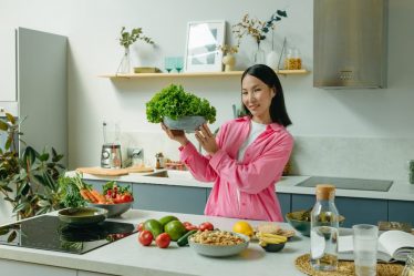Woman in a kitchen holding fresh lettuce, surrounded by healthy ingredients like tomatoes and avocados, promoting healthy eating.