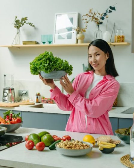 Woman in a kitchen holding fresh lettuce, surrounded by healthy ingredients like tomatoes and avocados, promoting healthy eating.