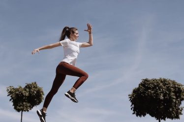 Athletic woman in action jump against a blue sky background. Captures fitness in motion.