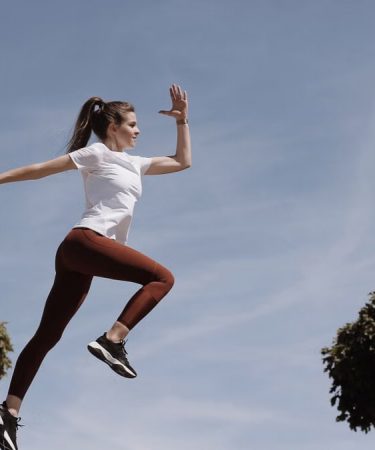 Athletic woman in action jump against a blue sky background. Captures fitness in motion.
