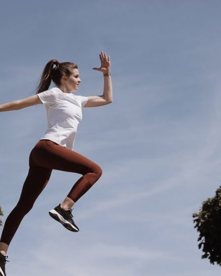 Athletic woman in action jump against a blue sky background. Captures fitness in motion.